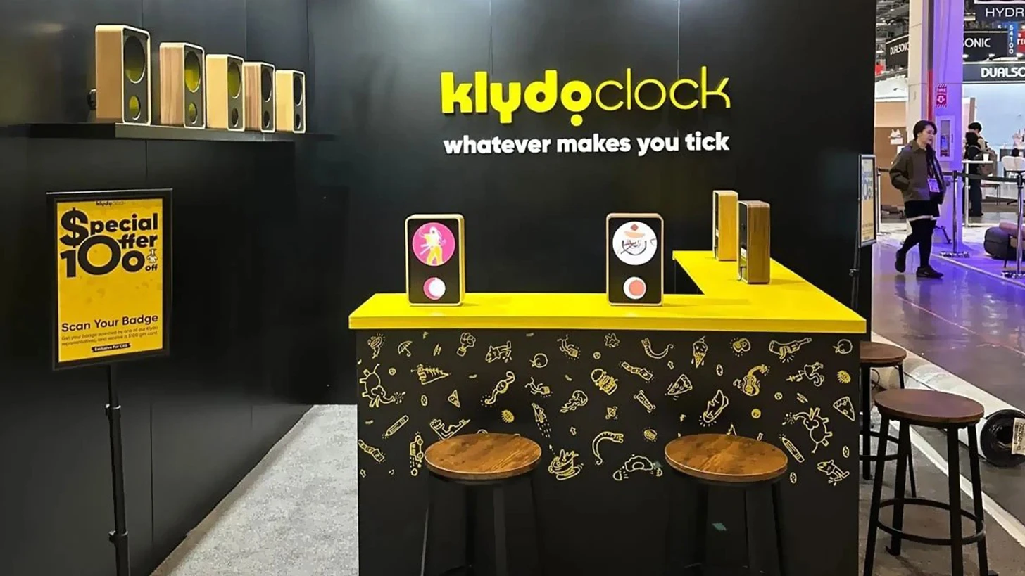 Black 10x10 Klydoclock booth with a yellow L-shaped counter, stools with wooden seats, and clock products on the counter and a wall shelf, built by Methodex at CES 2025