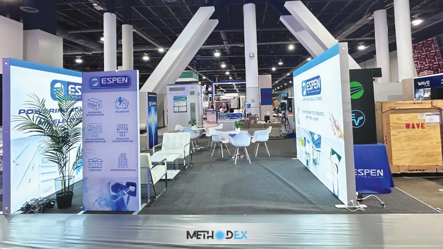 Espen Technology booth with backlit white and blue fabric walls, white lounge chairs, round tables, and a potted palm